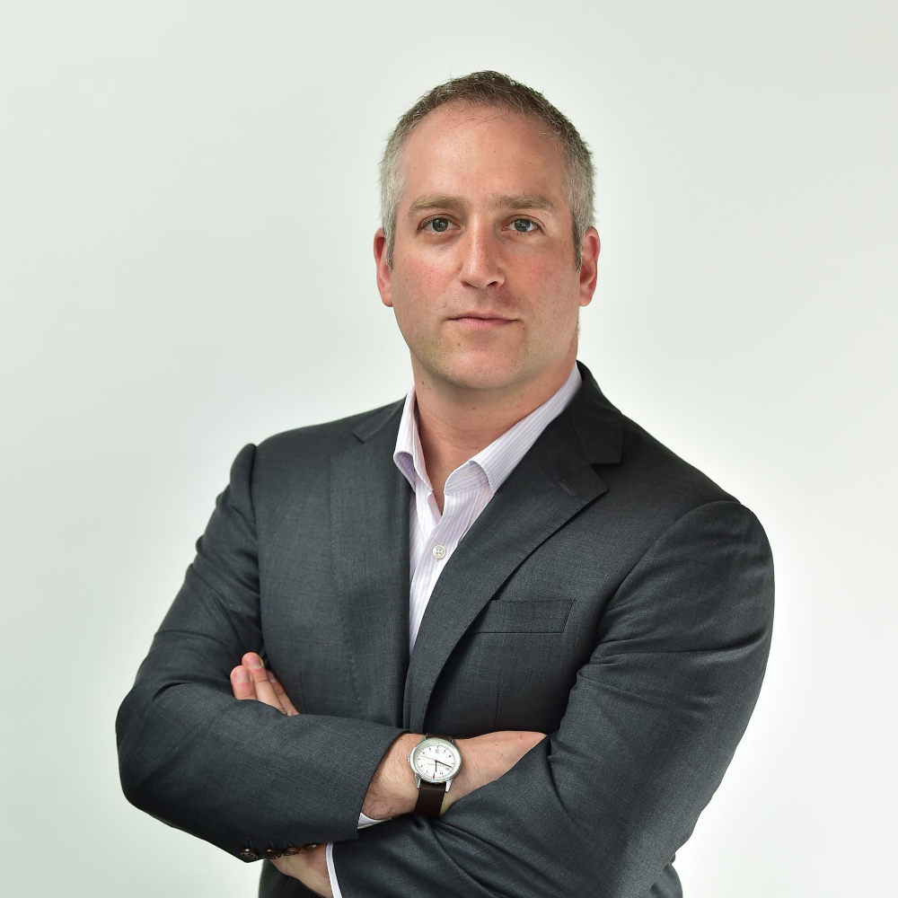 Founder of Buried in Work in a suit with arms crossed on a light gray background.